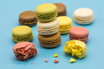 delicious macarons full and bitten and crumbs arranged on blue background