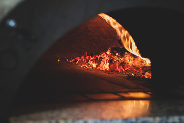 Toned dark photo of traditional oven for pizza with fire inside.