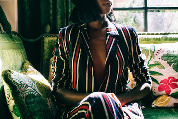 Anonymous Stylish Black Woman in Revealing Suit on Floral Velvet Sofa