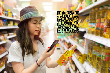 Young beautiful woman chooses a bottle of oil in the supermarket and checks the QR code on the...