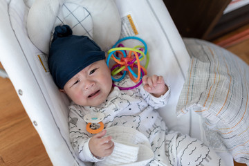 Annoyed cute asian baby with his teething toy in Bouncer