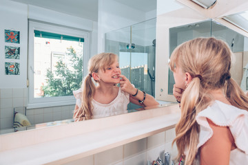 lovely blond child examining her healthy teeth in mirror in the bathroom