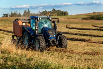 Blue tractor packs straw. Autumn work on the farm. Tractor on the field. Ecological agriculture.