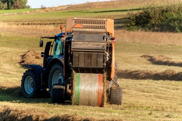 Plakat Blue tractor packs straw. Autumn work on the farm. Tractor on the field. Ecological agriculture.