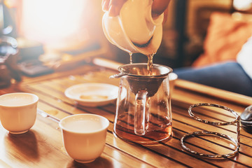 Chinese tea ceremony, girl pours pu-er from gaiwan through strainer in chahai, selective focus