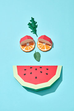 Smiling face made of paper pieces of watermelon, orange, apple and arugula leaves and mint on a blue background with copy space. Handcraft creative composition. Flat lay