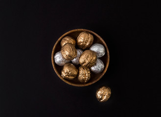 Painted golden and silver walnuts on wooden plate on black background