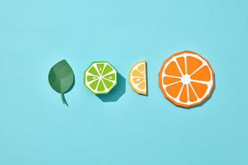 Set of lime, lemon and orange paper pieces with a mint leaf on a blue background with copy space. Handcraft composition. Flat lay