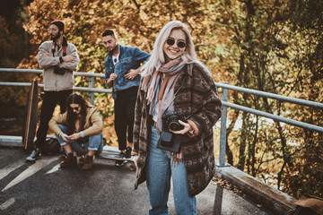 Happy smiling woman with photo camera is enjoying bright autumn day in park .