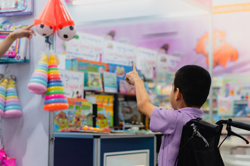 Disabled child on wheelchair trying begged parents to buy a toy for him in Books and toys fair,Special children's lifestyle,Life in the education age of special need kids,Happy disability kid concept.