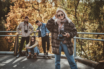 Smiling cheerful lady in sunglasses is posing for photographer while holding photo camera.