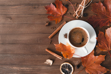 Cup of coffee with black coffee in a saucer on a wooden background, cinnamon,   red fallen autumn leaves, flat lay