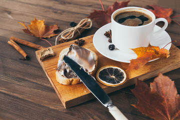piece of wheat bread with chocolate cream, a Cup of black coffee on the Board, autumn maple leaves,...