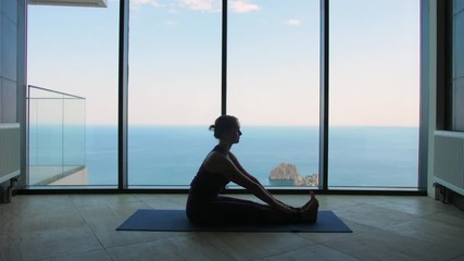 young woman doing yoga at the window overlooking the sea