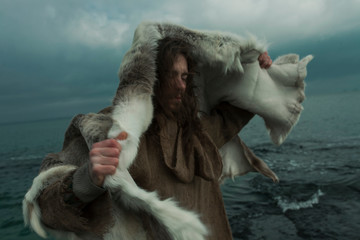 Young man with fur coat standing by sea