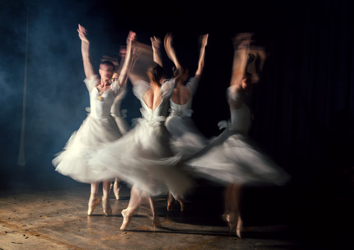 Ballerinas in dresses whirling on scene in darkness in fog