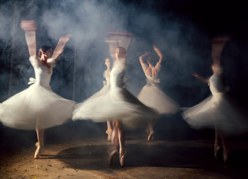 Ballerinas in dresses whirling on scene in darkness in fog