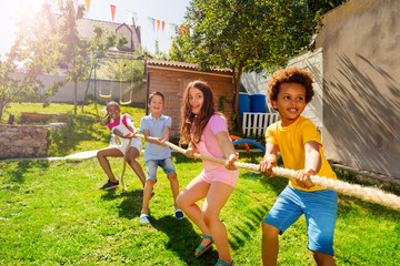 Group of kids play pulling rope game on the lawn