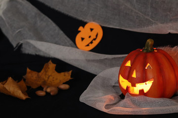 Jack pumpkin head on a dark background with gauze and decorations in the form of paper-cut bats and pumpkins. Burning candles. Withered yellow leaves. Halloween