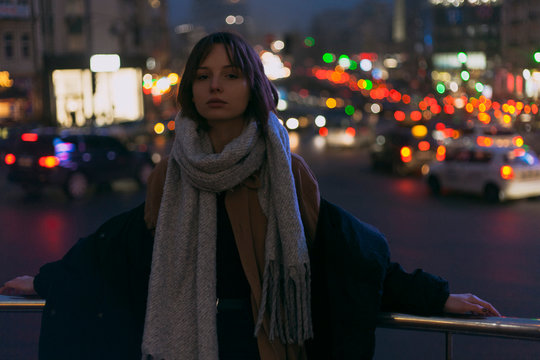 portrait of a beautiful girl in a jacket and scarf posing against the backdrop of the night road and the city