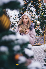 A young woman walks at Christmas in the square near the decorated Christmas trees. Candy is a lollipop in the form of a heart.