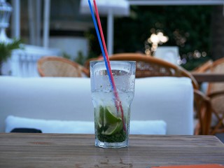 A glass of cold Mojito with ice is on the table on the summer veranda of the cafe. The glass with the tube is covered with droplets of condensate. Drink on a hot summer day.