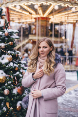 A young woman walks at Christmas in the square near the decorated Christmas trees. Candy is a lollipop in the form of a heart.