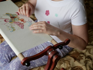 Fototapeta premium a young woman with beautiful hair in a white t-shirt embroiders colorful butterflies on a special wooden machine. Multicolored floss on a white canvas.