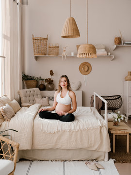 Happy young woman in expectancy sitting on bed