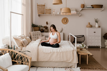 Happy young woman in expectancy sitting on bed