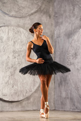 Full body portrait. Russian ballerina in a black dancing suit is posing in dark studio