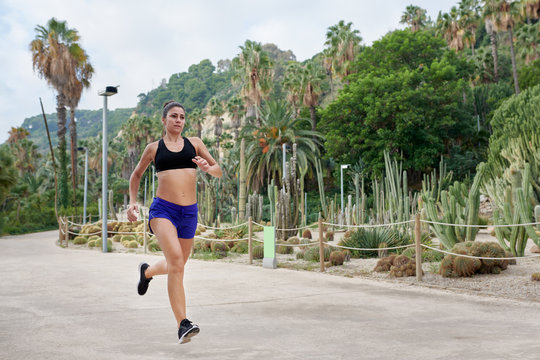 Confident sportswoman jogging in green tropical park