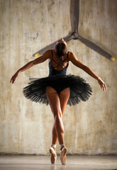 Full body portrait. Russian ballerina in a black dancing suit is posing in dark studio