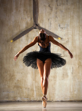 Full body portrait. Russian ballerina in a black dancing suit is posing in dark studio