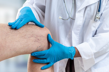 Close-up image of female doctor cheking knee of male patient