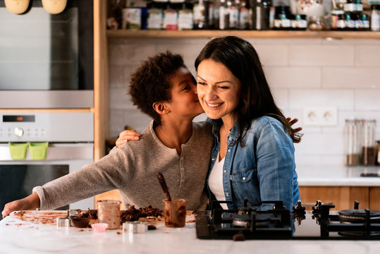 Happy black child kissing his mother in the kitchen