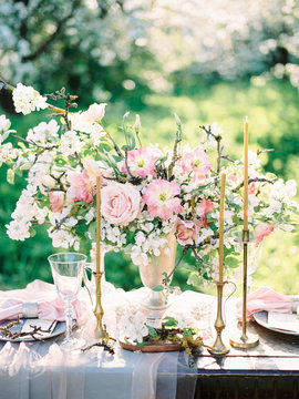 Festive served table with flower arrangement of twigs of blossoming apple tree and roses