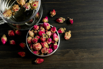 dried rose buds tea in metal container accompanied by glass mug on wood background