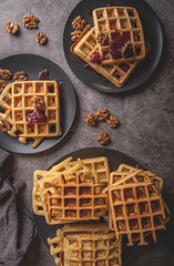 Plates of belgian waffles with strawberry jam and walnuts on dark gray background flat lay top view