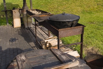 Wooden platform for cooking outdoors with a rusty barbecue, a cauldron for cooking pilaf with a wooden barrel and firewood