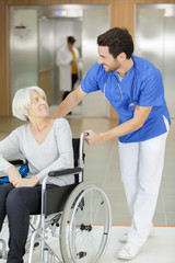Obraz premium side view of social worker pushing wheelchair with senior woman