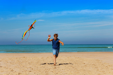 Handsome boy in blue shirt run with kite near sea