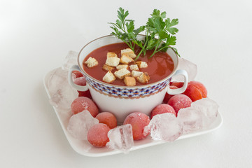 Summer cold tomato soup (gazpacho). Ice and frozen tomatoes on a plate, white background.