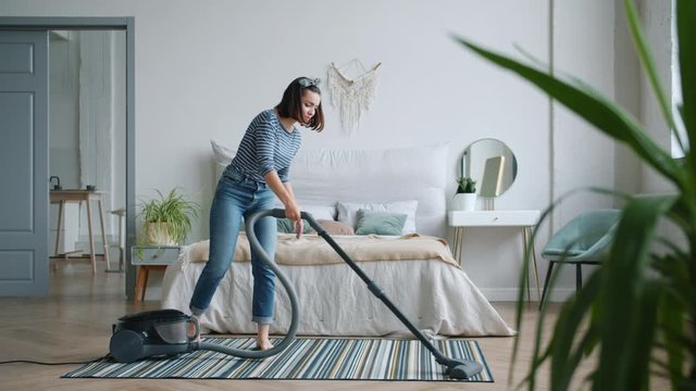 Young housewife attractive young girl is vacuuming floor in bedroom using vacuum cleaner working alone wearing casual clothing. People and housework concept.