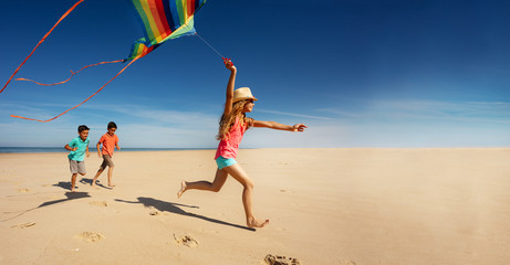 Girl and friends run fast on beach hold color kite