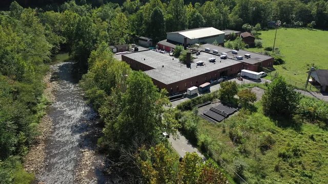 Aerial pull back showing the Marsh Fork Elementary School next to a river with Montcoal mining operation with coal slurry pipelines in mountains of West Virginia.
