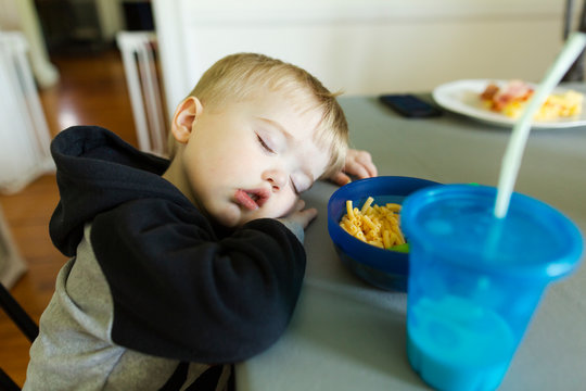 Close-up of blonde toddler boy sleeping with head on table at lunch
