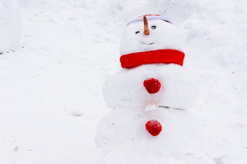 Snowman standing on the background of white snowdrifts in the winter landscape. A lot of snow. Snowman with a red hat, scarf and buttons.