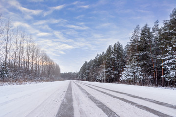 Fototapeta premium Patterns on the winter highway in the form of four straight lines. Snowy road on the background of snow-covered forest. Winter landscape.