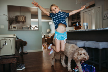 Girl jumping for joy in kitchen with dogs